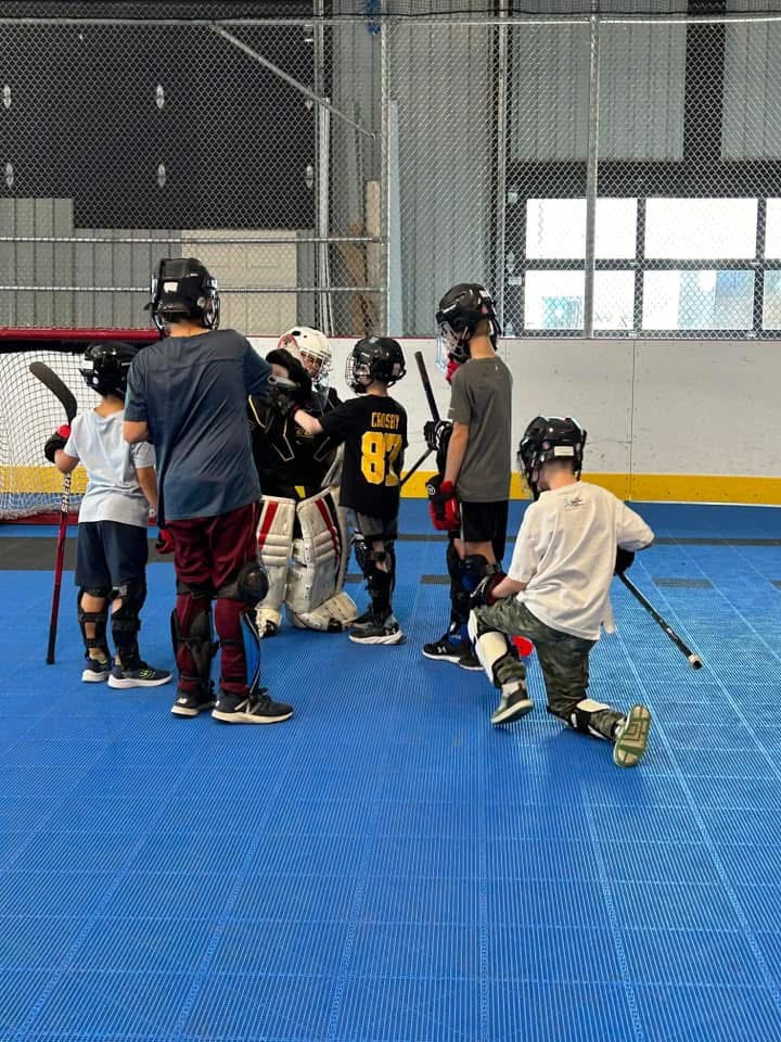 Des jeunes joueurs de dek hockey se rassemblent près du but au camp