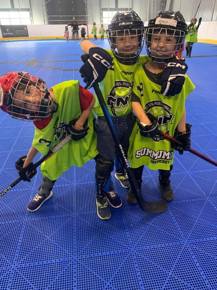 Trois jeunes campeurs équipés pour le dek hockey sur la surface intérieure du DHG